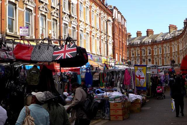 Market stalls lined along Electric Avenue at Brixton Market with shoppers and Victorian shopfronts