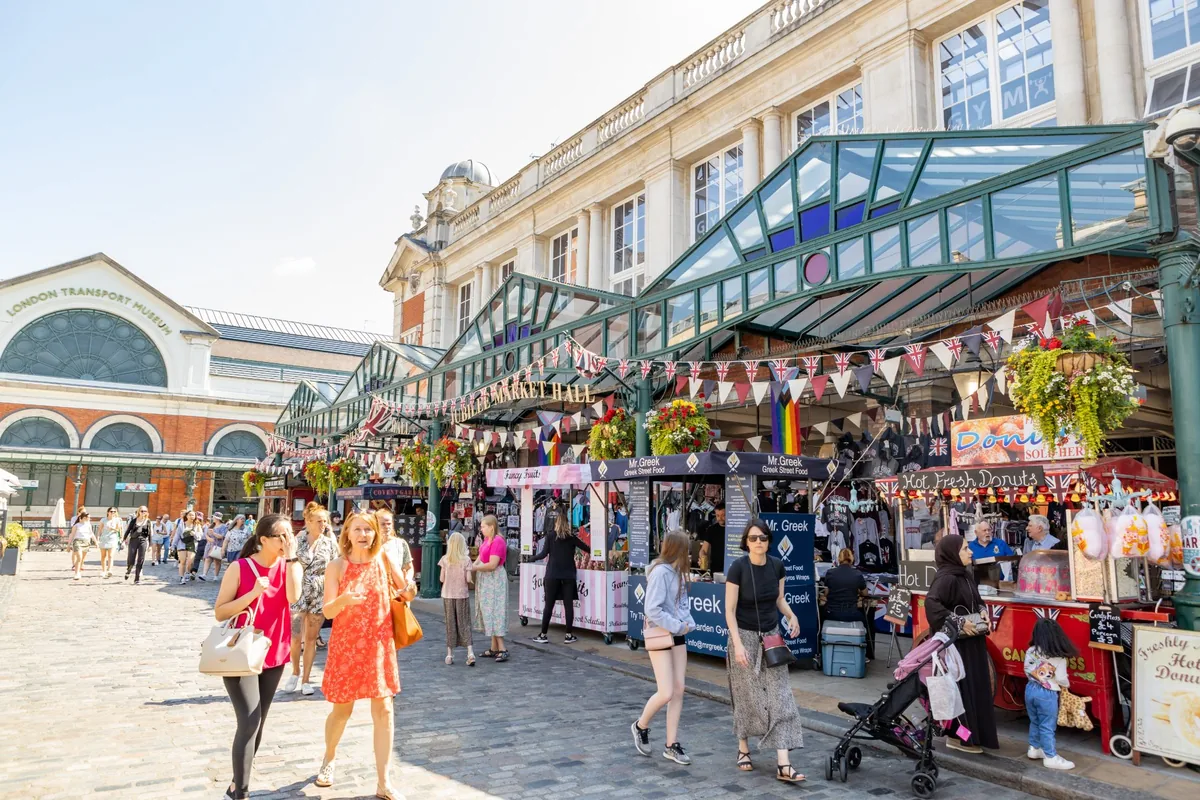 Stalls with flags and bunting at the entrance to Jubilee Market on the Covent Garden Piazza, with shoppers walking past