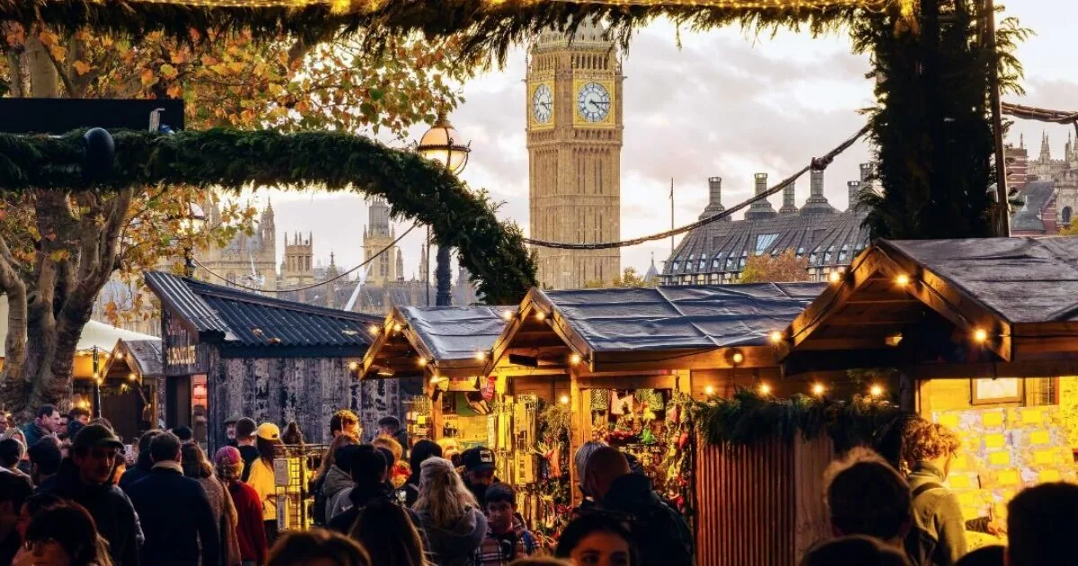 Wooden Southbank Centre Winter Market chalets with festive lights and crowds on Queen's Walk, Big Ben behind, at dusk