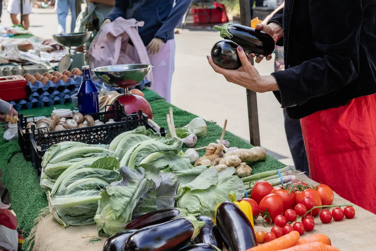 Vegetable stall at Stepney Farmers' Market with cabbages, tomatoes and aubergines and a customer choosing produce